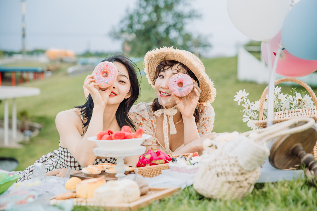 野餐郊游白天吃甜甜圈的闺蜜户外草地趴在草地上摄影图配图图片