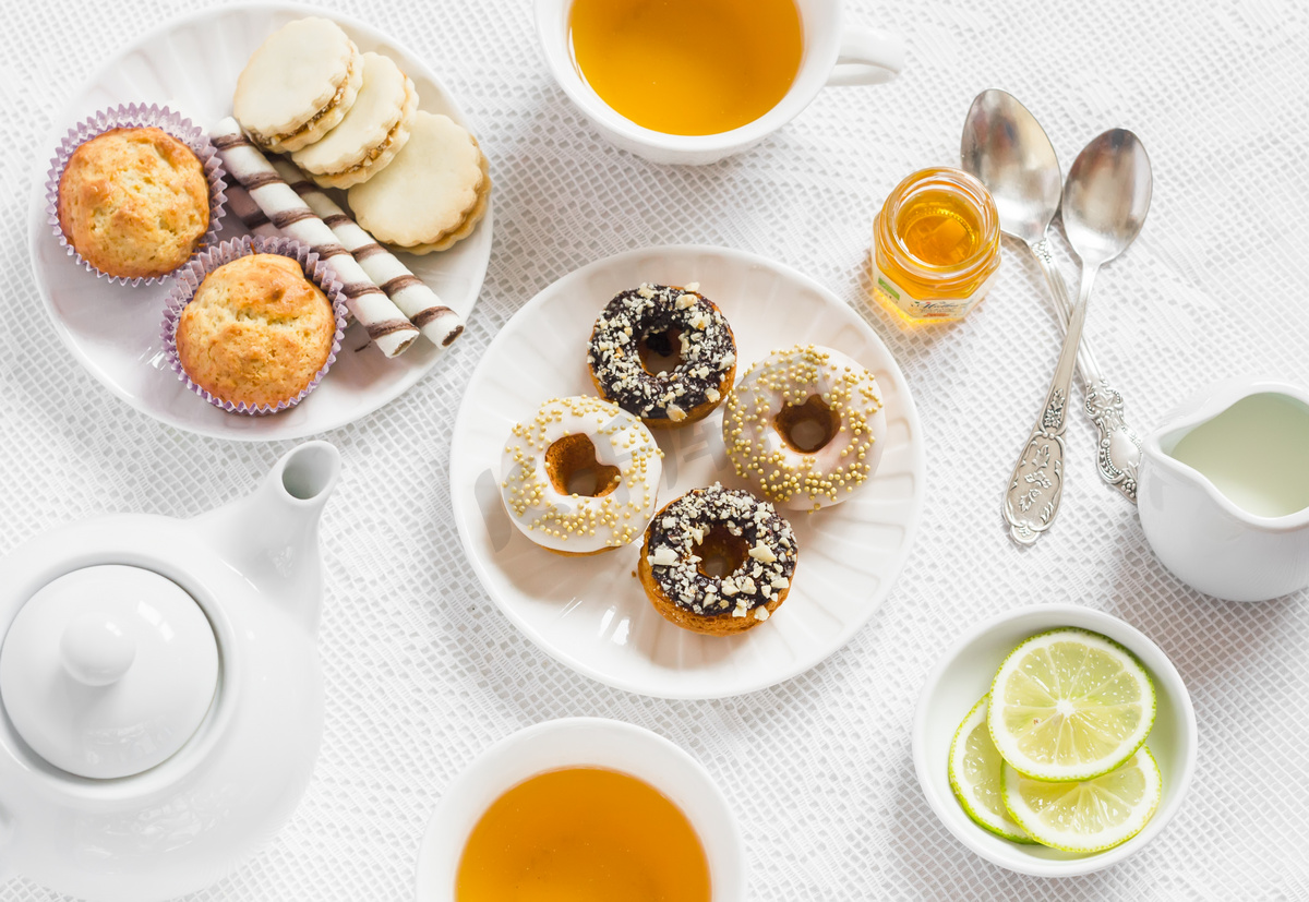 柠檬绿茶和糖果-香蕉松饼，饼干和巧克力焦糖和坚果，甜甜圈和柠檬釉茶具在白色桌布上光的表面上。下午茶。葡萄酒和乡村风格图片