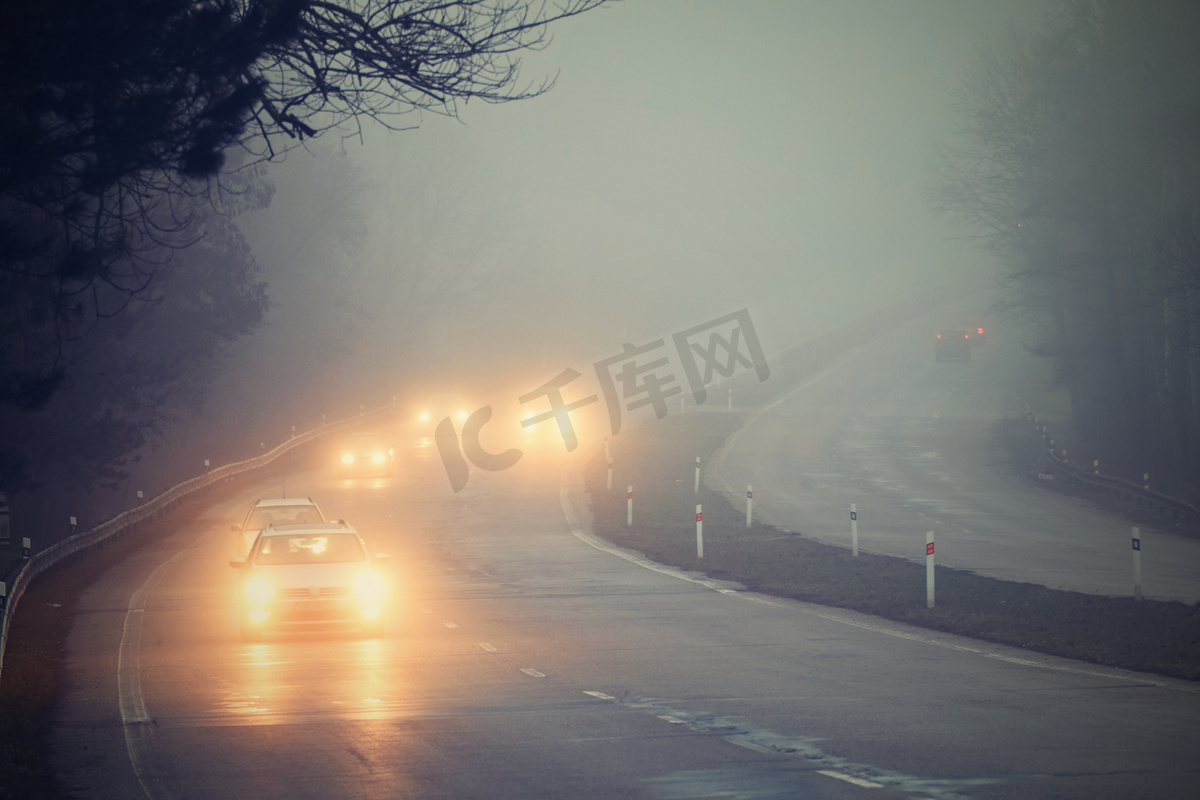 汽车在雾中。恶劣的冬季天气和路上危险的汽车交通。雾中的轻型车辆.图片