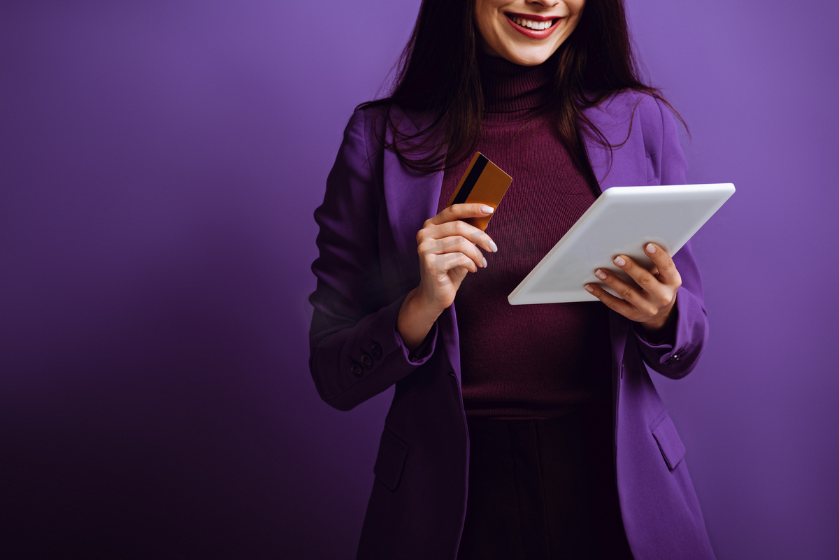 带着紫色背景的数码平板电脑和信用卡微笑的女人的剪影图片