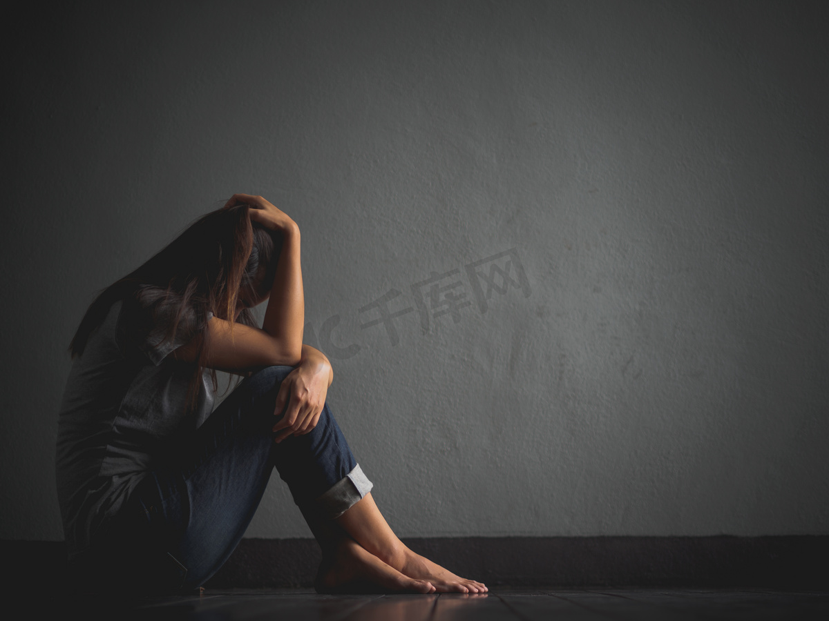 悲伤的女人抱着她的膝盖和哭泣。悲伤的女人独自坐在空荡荡的房间.图片