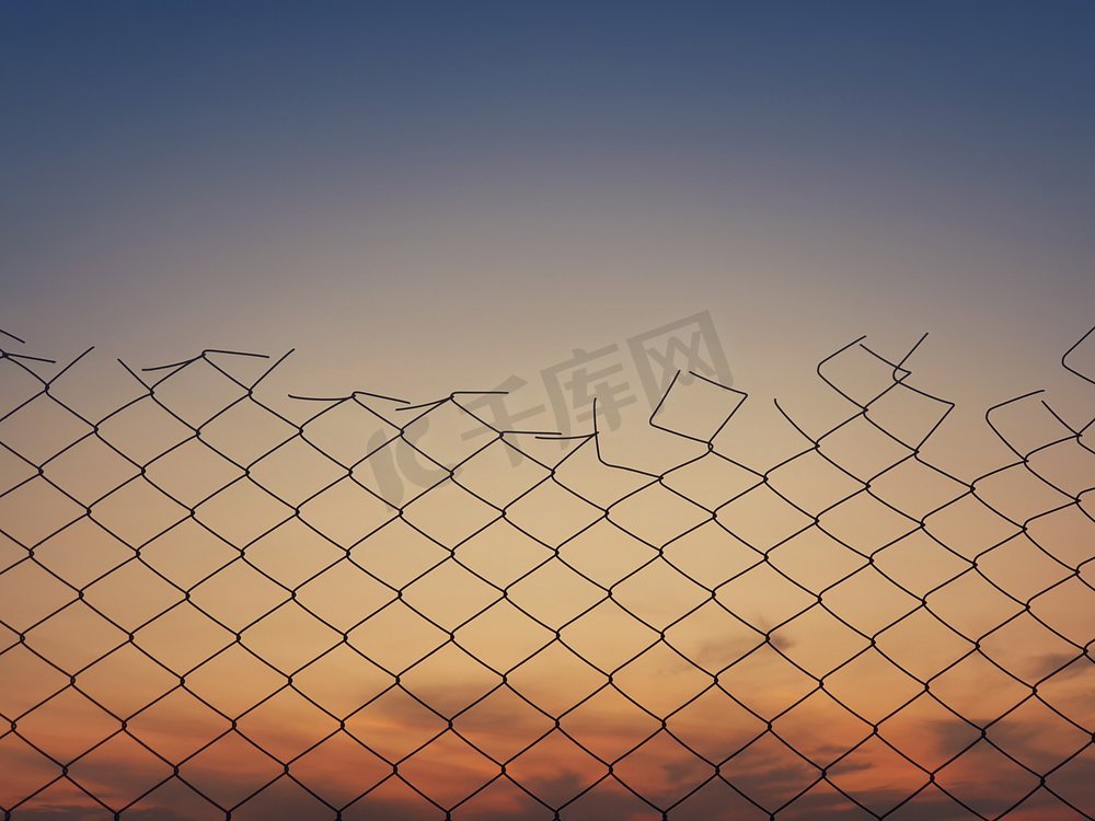 老铁丝网栅栏纹理反对日落天空背景。图片