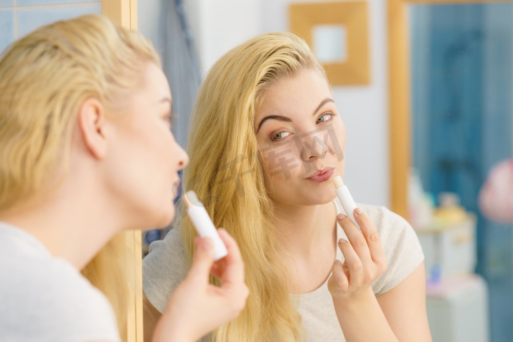 金发女人在浴室里放应用润唇膏保湿香脂，照顾她的嘴唇皮肤。妇女在浴室应用唇膏图片