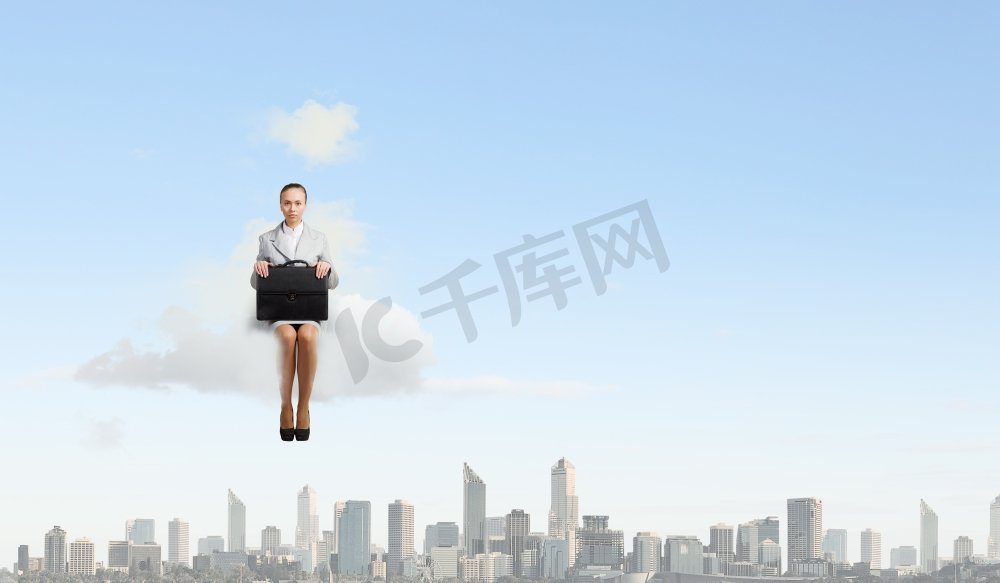 云上的女人。年轻漂亮的女商人坐在城市上空的云端图片