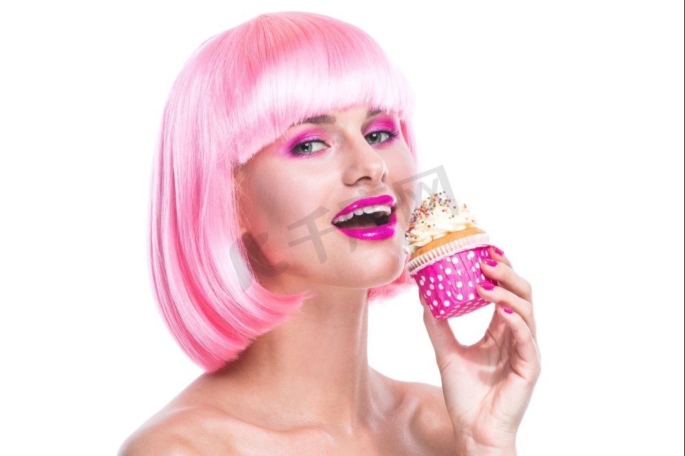 拿着蛋糕的魅力女孩。画中的女孩化着迷人的妆，留着粉色的头发，准备吃白色背景下孤立的蛋糕图片