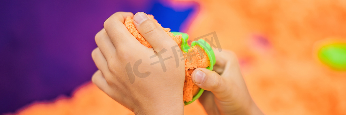 男孩的手在玩橙色动感沙 BANNER, LONG FORMAT图片