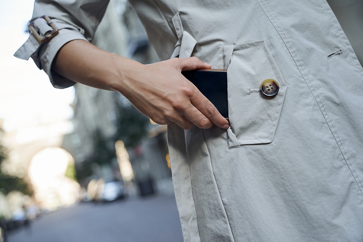一位身穿灰色外套的女士站在户外将智能手机放入口袋的裁剪镜头图片