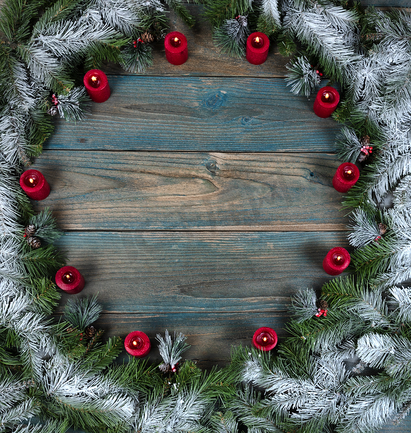 圣诞节或新年背景的冬季假期期间，蓝色老化木板上的圆形边框上有一个雪覆盖的花环，上面有发光的红色蜡烛装饰品图片
