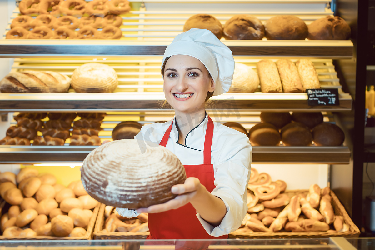 穿着围裙的女售货员在面包店里展示新鲜面包图片