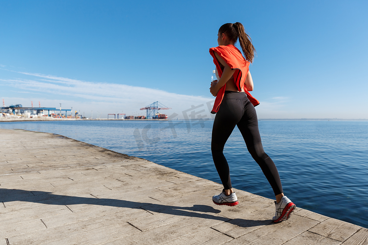 沿着海滨长廊跑步的活跃健康健身女性的后视图。图片