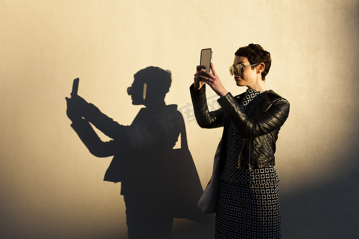 中年妇女用智能手机自拍身旁墙上投下阴影图片