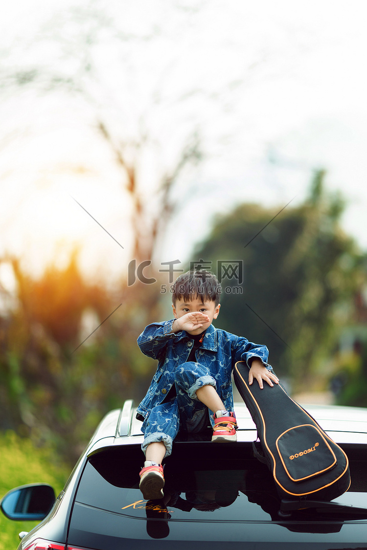 手拿吉他坐在车顶的男孩摄影图配