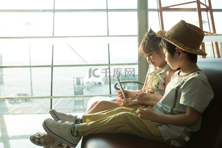 两个小朋友坐在机场候车厅看平板