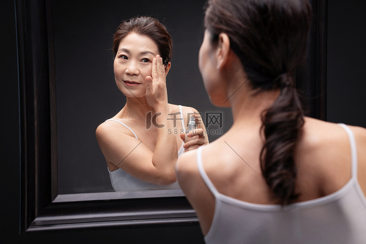 优雅的中年女人对着镜子涂抹爽肤