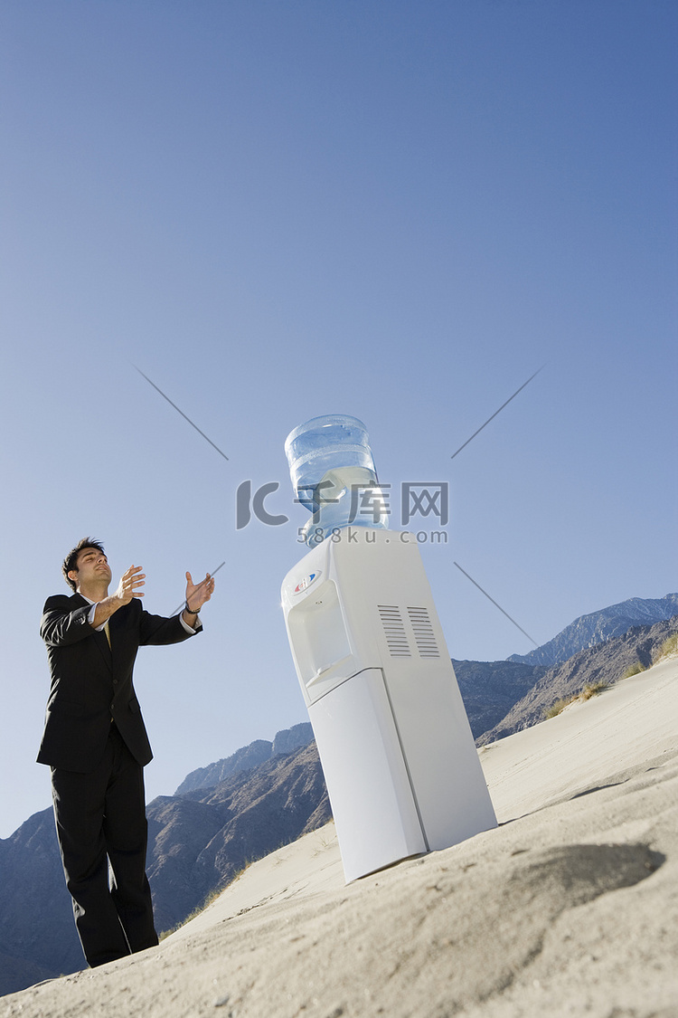 在沙漠中站在水冷却器旁的商人
