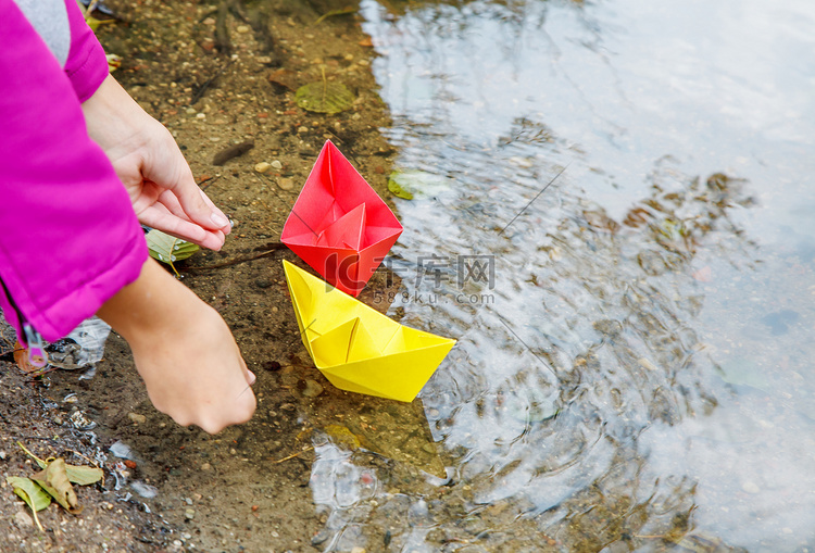 女孩把两只彩色纸船放在小溪里