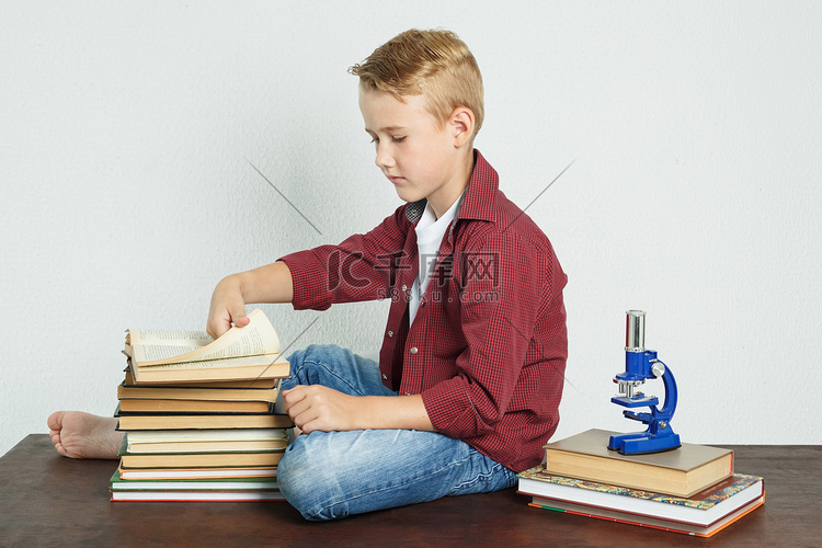 男学生坐在靠近书本的桌子旁，翻