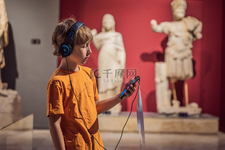 男孩在博物馆展览中观看雕塑并听