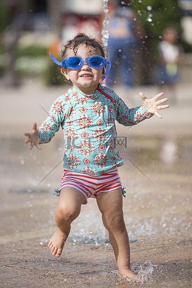 女孩戴着泳镜在喷泉里玩耍笑着看