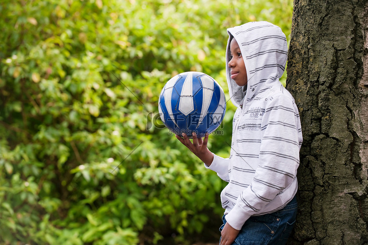 男孩抱着球靠在树上