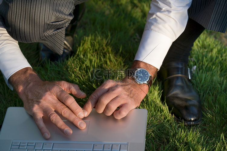 一名男子用笔记本电脑蹲在草地上