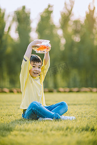 草地上端着金鱼的小男孩