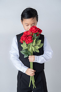 情人节白天穿西装帅气男童室内手拿玫瑰低头闻花摄影图配图