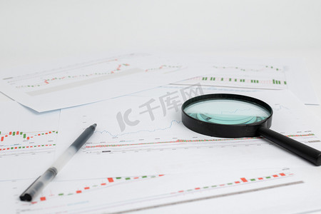 桌子桌面摄影照片_商务金融棚拍股票图表上对放大镜股票概念静物摄影图配图
