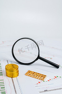 金币摄影照片_商务金融棚拍股票图表上对放大镜金币算盘室内竖图摄影图配图