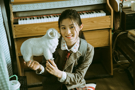 美女学生白天一个女学生在钢琴室手拿小羊看镜头笑摄影图配图