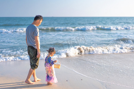 海面海水摄影照片_沙滩散步的父女傍晚父女沙滩侧面摄影图配图