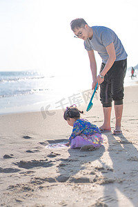 平静的海面摄影照片_海边的父女傍晚父女挖沙亲子时光摄影图配图