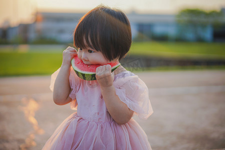 吃西瓜的小女孩夕阳女孩草地吃瓜摄影图配图