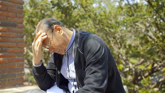 卡通男孩坐在西瓜上吃西瓜摄影照片_老人独坐在户外头部疼痛揉搓疾病身体不适症状人像