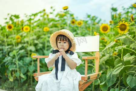 夏天吃糖摄影照片_儿童孩子女童花海傍晚儿童两岁向日葵正面吃棒棒糖摄影图配图