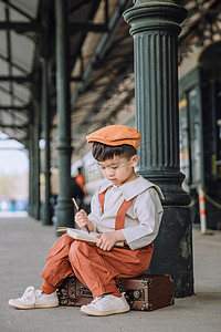 儿童文艺白天小男孩户外火车站低头坐着写字摄影图配图