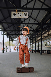 文艺儿童白天小男孩户外火车站踩着行李箱玩耍摄影图配图