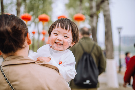 妈妈摄影照片_亲子白天妈妈抱着女儿户外公园抱着走路摄影图配图