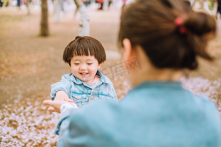 小孩伸手摄影照片_亲子白天妈妈和女儿户外樱花树伸手摄影图配图