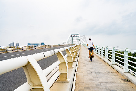运动白天骑行的男生的背景户外桥上骑车摄影图配图