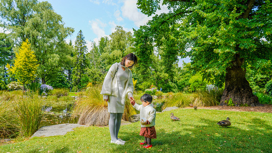 小朋友抱着小鸭子摄影照片_喂鸭母女下午太阳夕阳母女公园喂鸭子全身摄影图配图