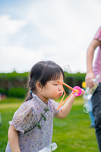 儿童泡泡摄影照片_吹泡泡的女孩下午儿童户外草地半身照嘟嘟嘴摄影图配图