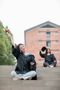 毕业季白天穿着学士服的美女毕业生户外举起毕业证摄影图配图
