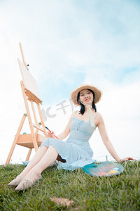 文艺清新白天穿着白裙子的写生美女户外坐在草地上摄影图配图