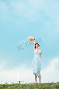 文艺清新白天穿着白裙的美女户外草坪挥动帽子摄影图配图