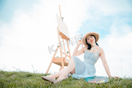 文艺清新白天穿着白裙子的写生美女户外草坪坐在草地上摄影图配图
