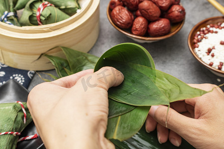 端午佳节摄影照片_端午节美食白天裹粽子室内美食摆拍摄影图配图