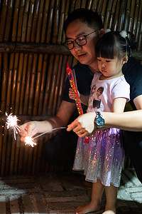 孩子烟花摄影照片_玩烟花的父女夜晚父女室外半身摄影图配图