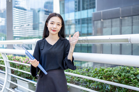 商务金融白天商务女青年人行桥拿文件夹打招呼摄影图配图