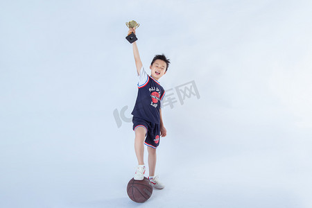 背景人物摄影照片_获奖的孩子白天一个男孩室内白背景手拿奖杯脚踩球摄影图配图